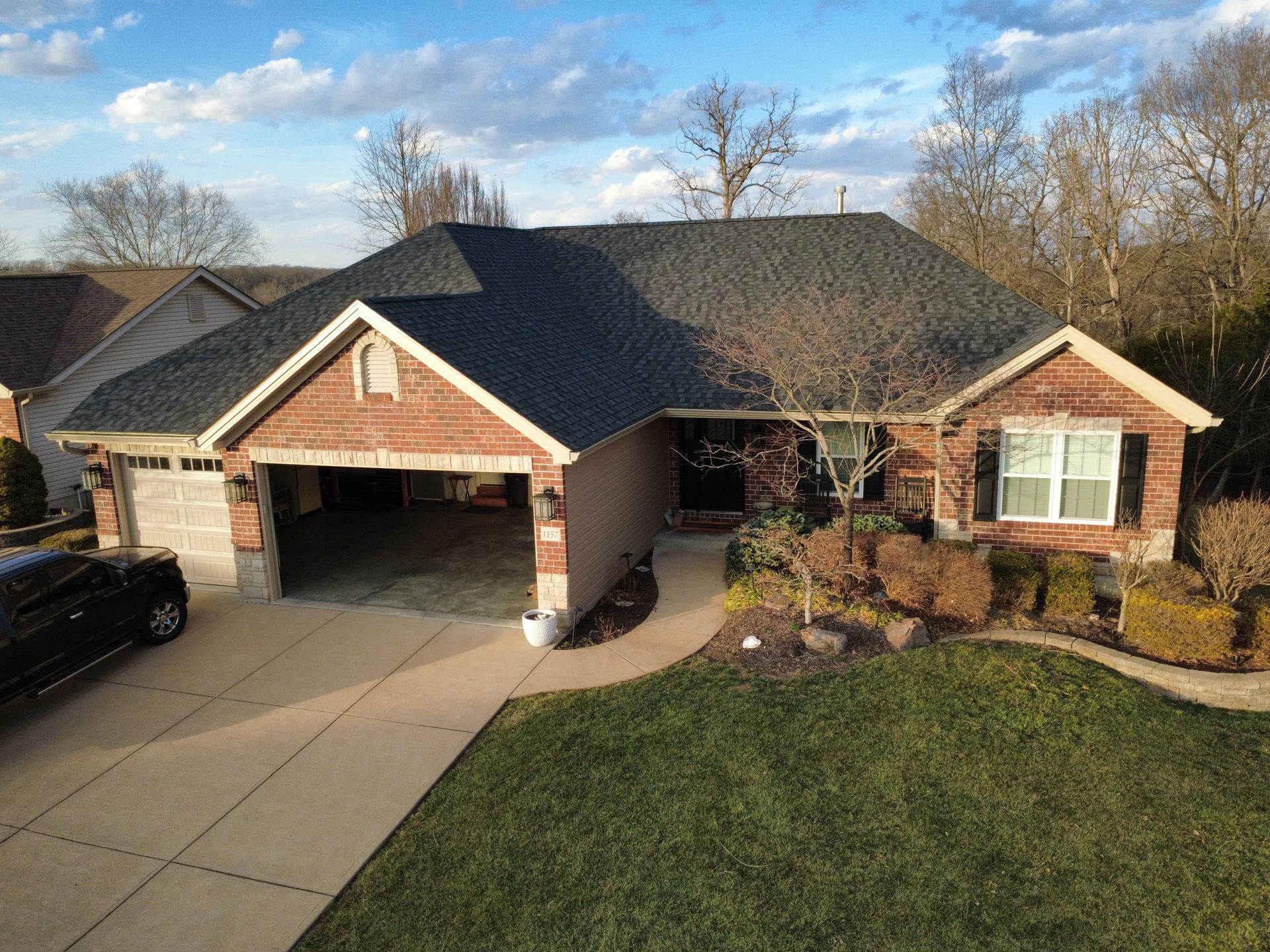 A single-story brick house with a gray shingled roof, a two-car garage, and a manicured lawn under a sunny sky.