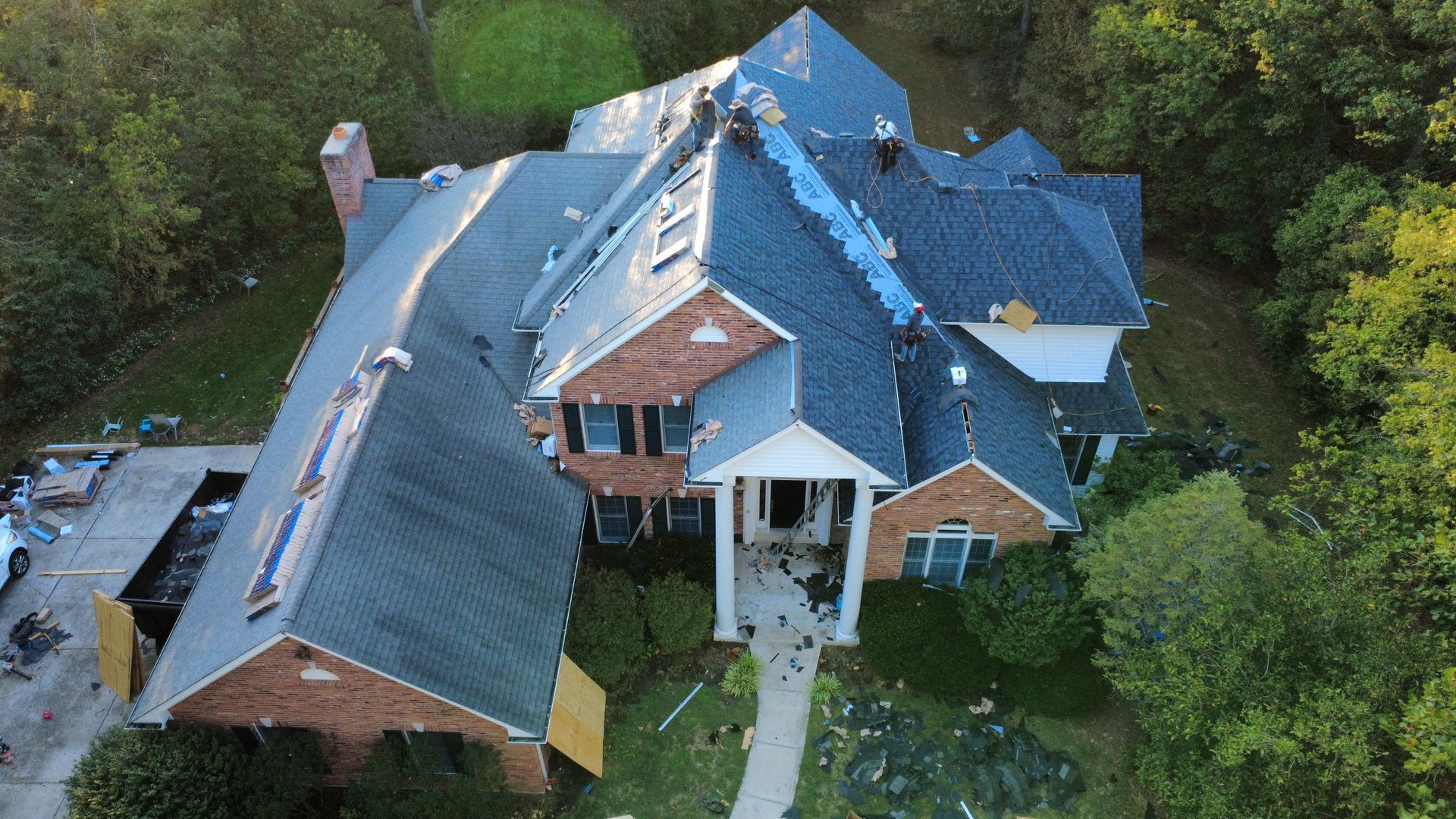 Aerial view of a multi-story brick home under roof construction, with exposed wood decking and debris on the ground.