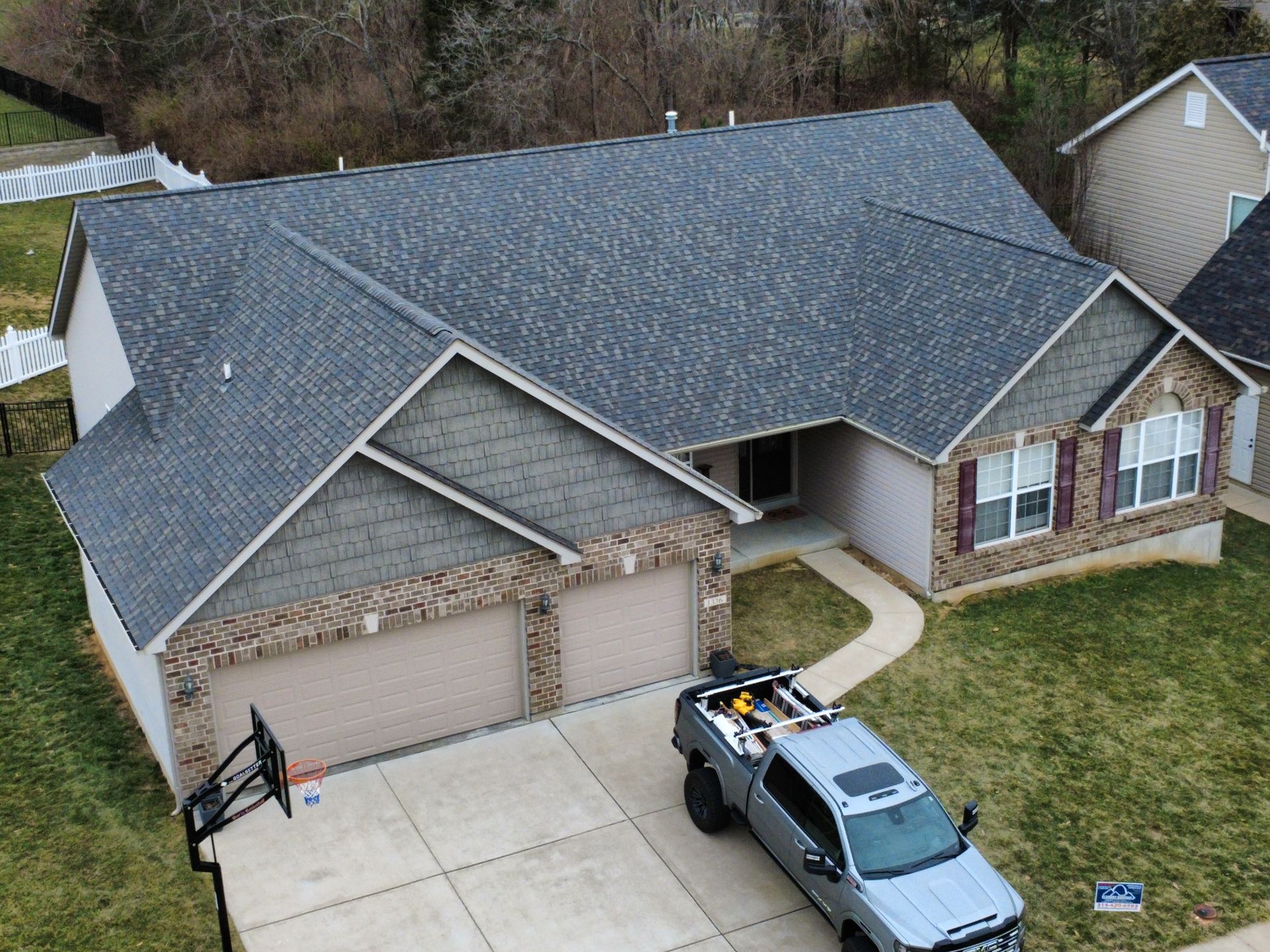 A suburban home with a gray shingled roof, brick trim, and a gray pickup truck parked in the driveway.