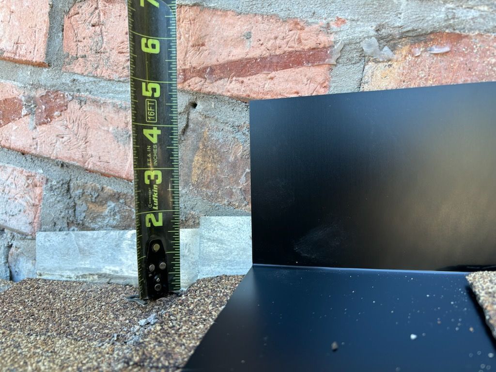 Measuring tape beside a brick wall, black panel, and gravel ground outdoors.