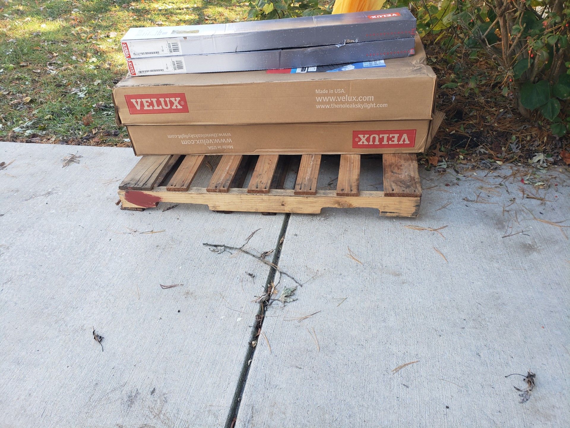Two stacked Velux boxes and a long tube sit on a wooden shipping pallet placed on a concrete sidewalk.