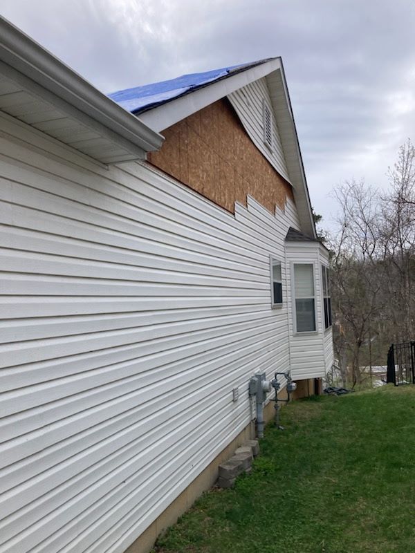 Side view of a house exterior showing exposed plywood sheathing on the upper gable wall where siding is missing.