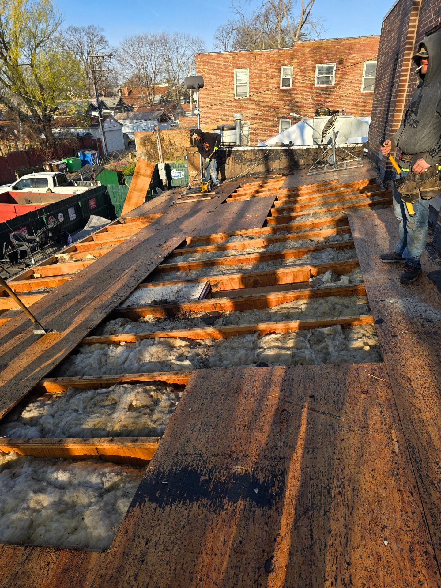 Construction workers remove plywood roof decking, exposing the wooden joists and insulation of a building under renovation.