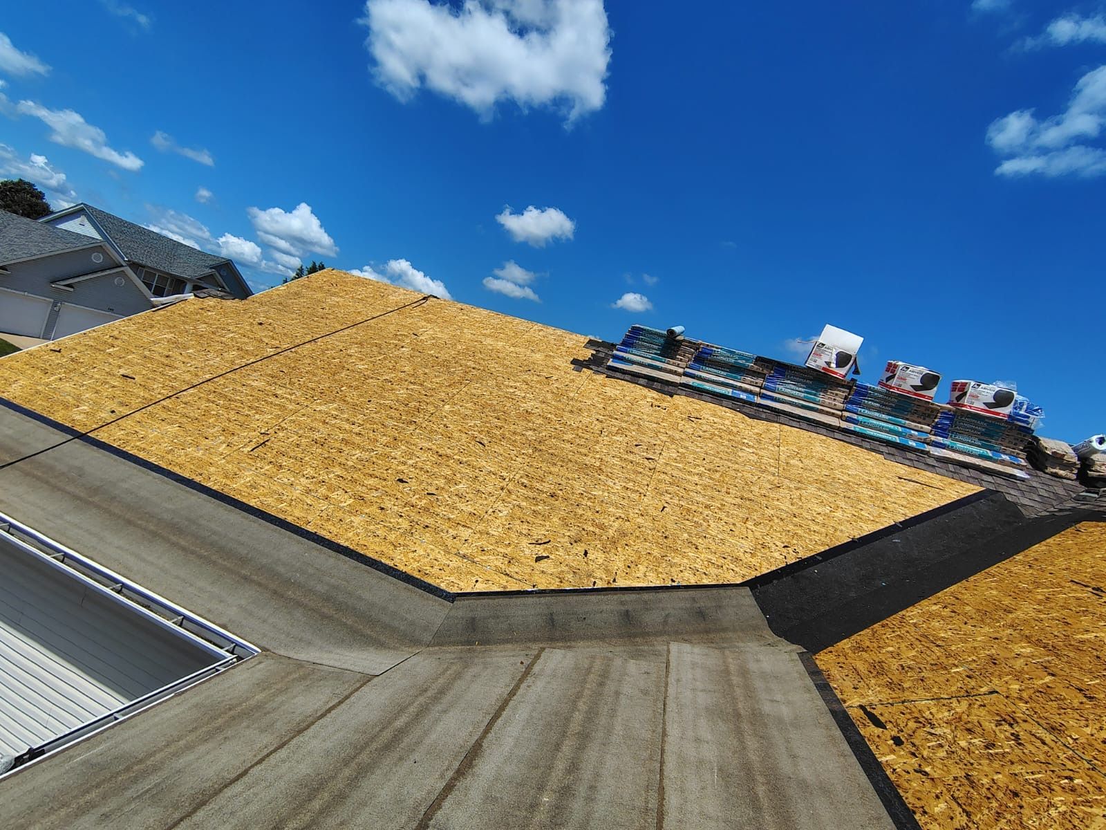 A roof under construction featuring exposed wood decking alongside sections covered in grey underlayment under a blue sky.