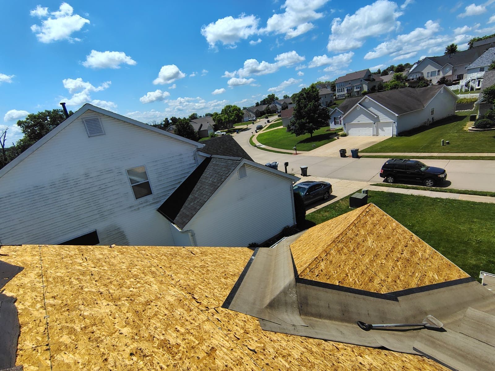 High-angle view of a house roof undergoing construction with exposed wooden decking and adjacent neighborhood houses.