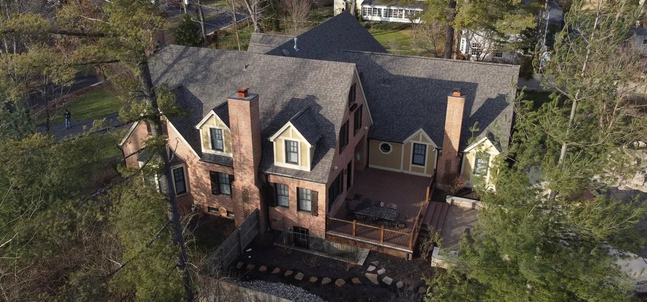 Aerial view of a large brick house with a steep gray roof and surrounding trees.