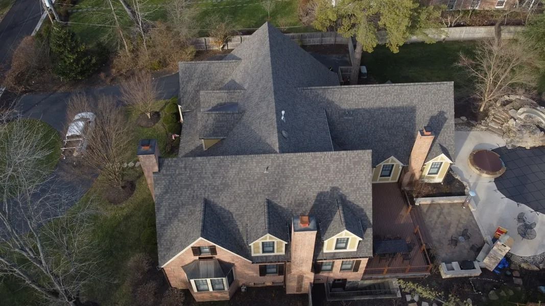 Aerial view of a large brick house with a gray roof and surrounding trees