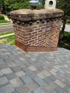 Brick mailbox pillar beside a gray paver driveway and lawn