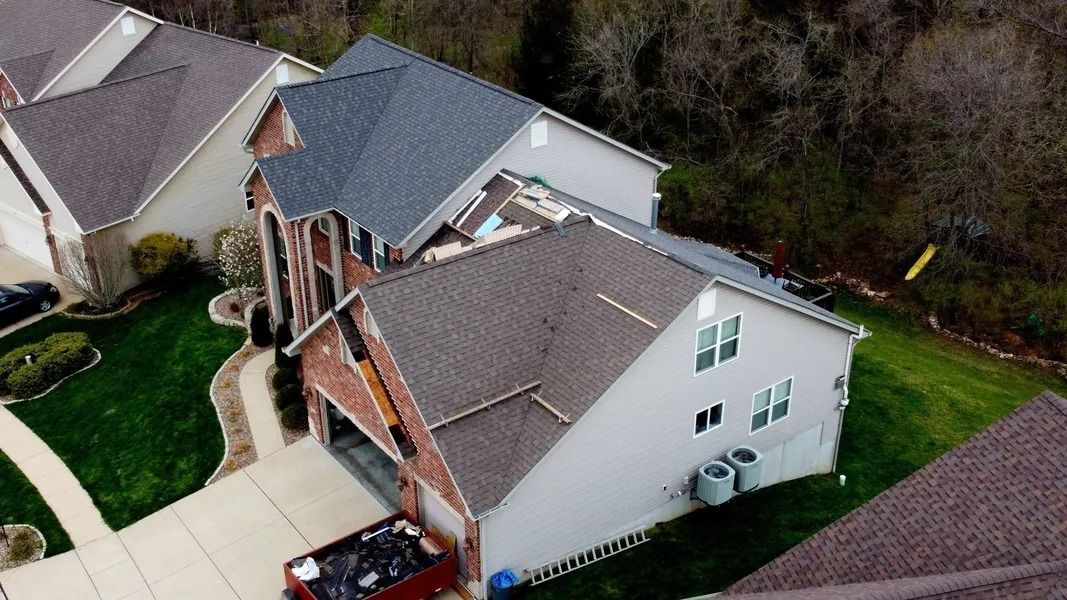 Aerial view of a residential home with significant roof damage and a dumpster in the driveway.
