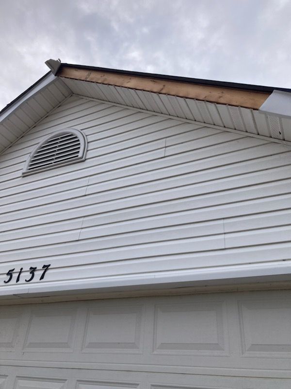 A close-up view of the white vinyl-sided gable of a garage, showing a missing section of trim along the wooden roofline.