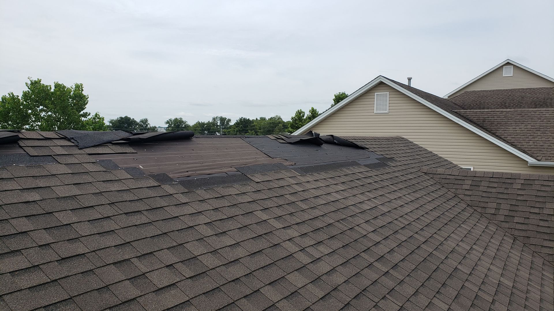 Damaged shingle roof with visible holes and missing sections near a beige house