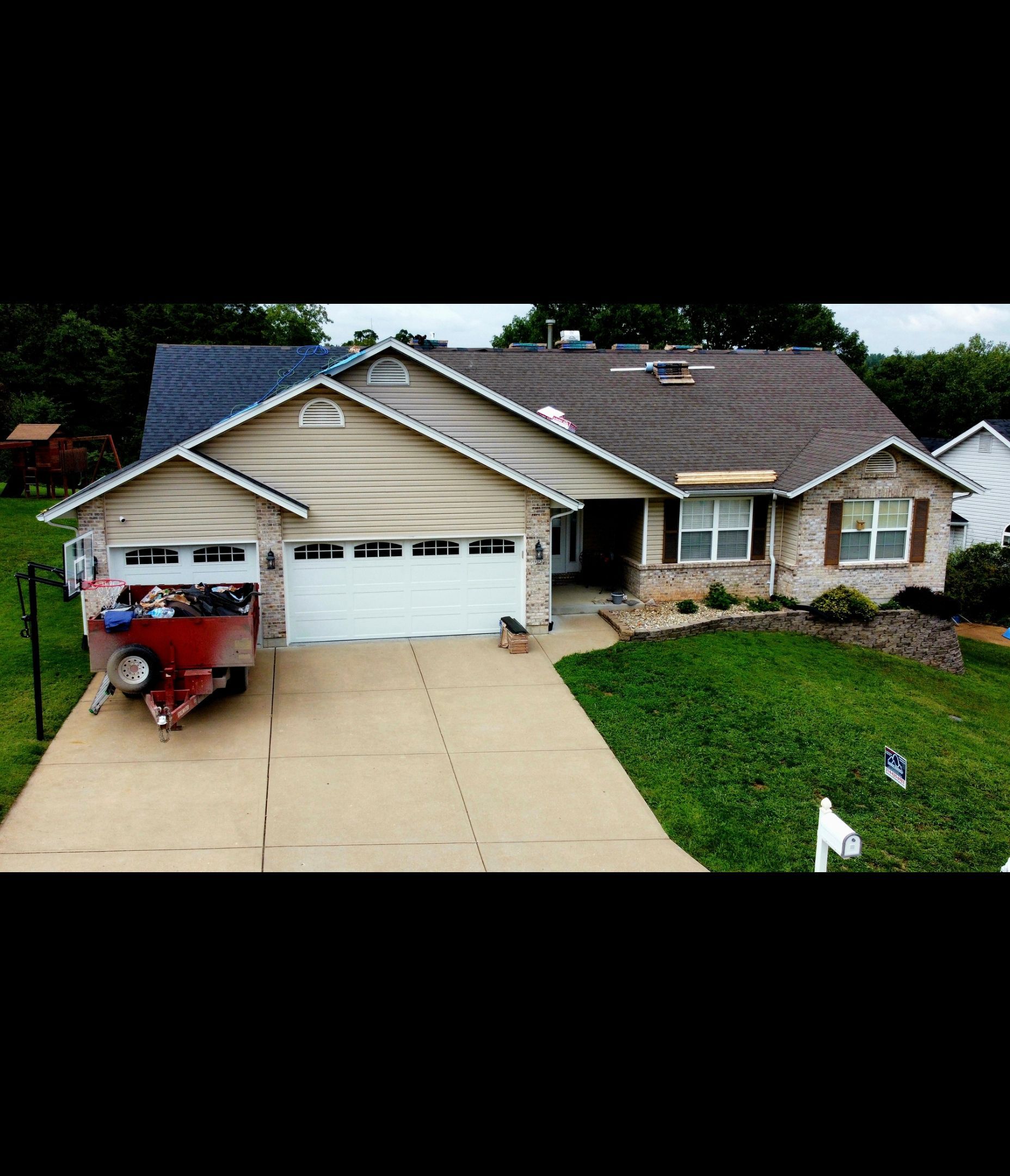 A single-story tan house with a multi-gabled roof and a two-car garage, featuring a red boat trailer parked in the driveway.