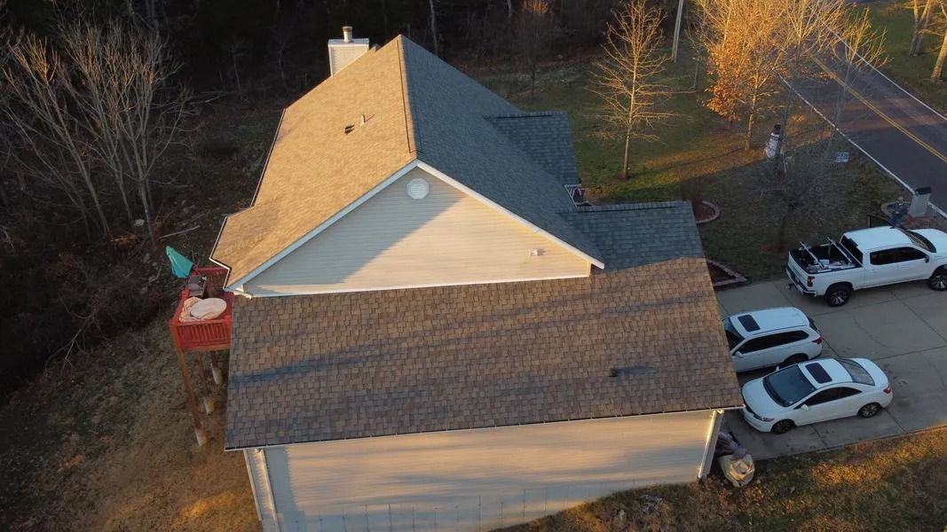 Aerial view of a house with a dark roof, tan walls, and several white cars parked beside it.