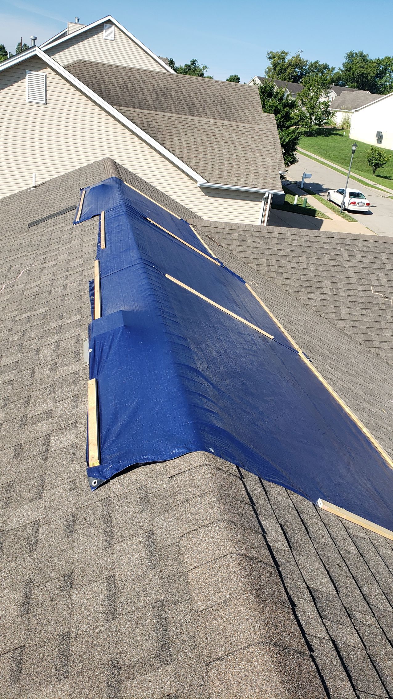 Blue tarp-covered section on a shingled residential roof with a roof valley repair area.