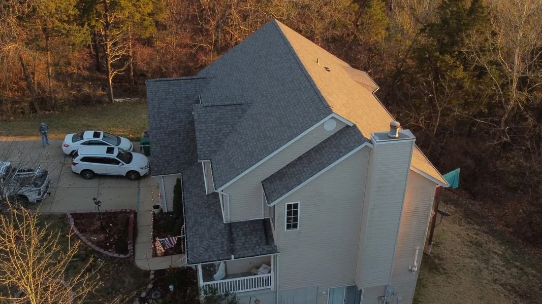 An aerial view of a suburban two-story home with a gray shingled roof, beige siding, and two cars parked in the driveway.