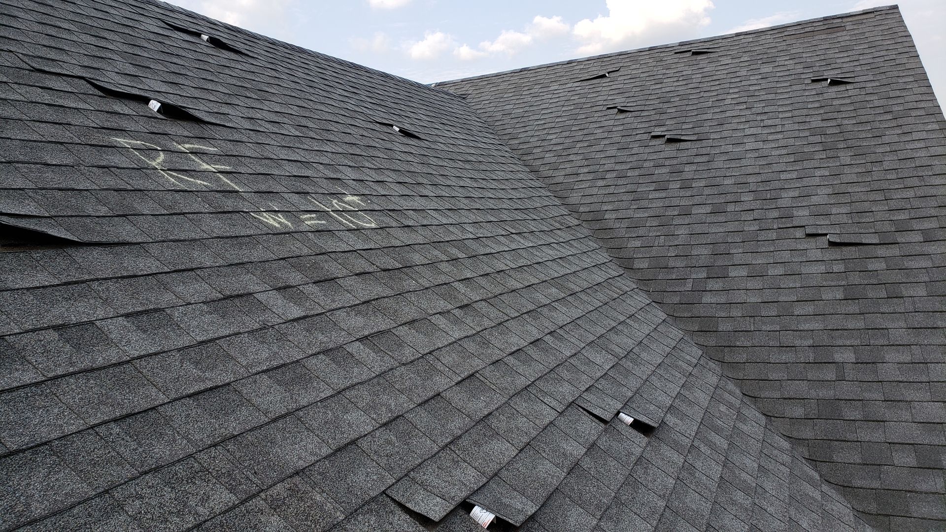 Gray shingled roof with intersecting slopes and several small roof vents under a cloudy sky