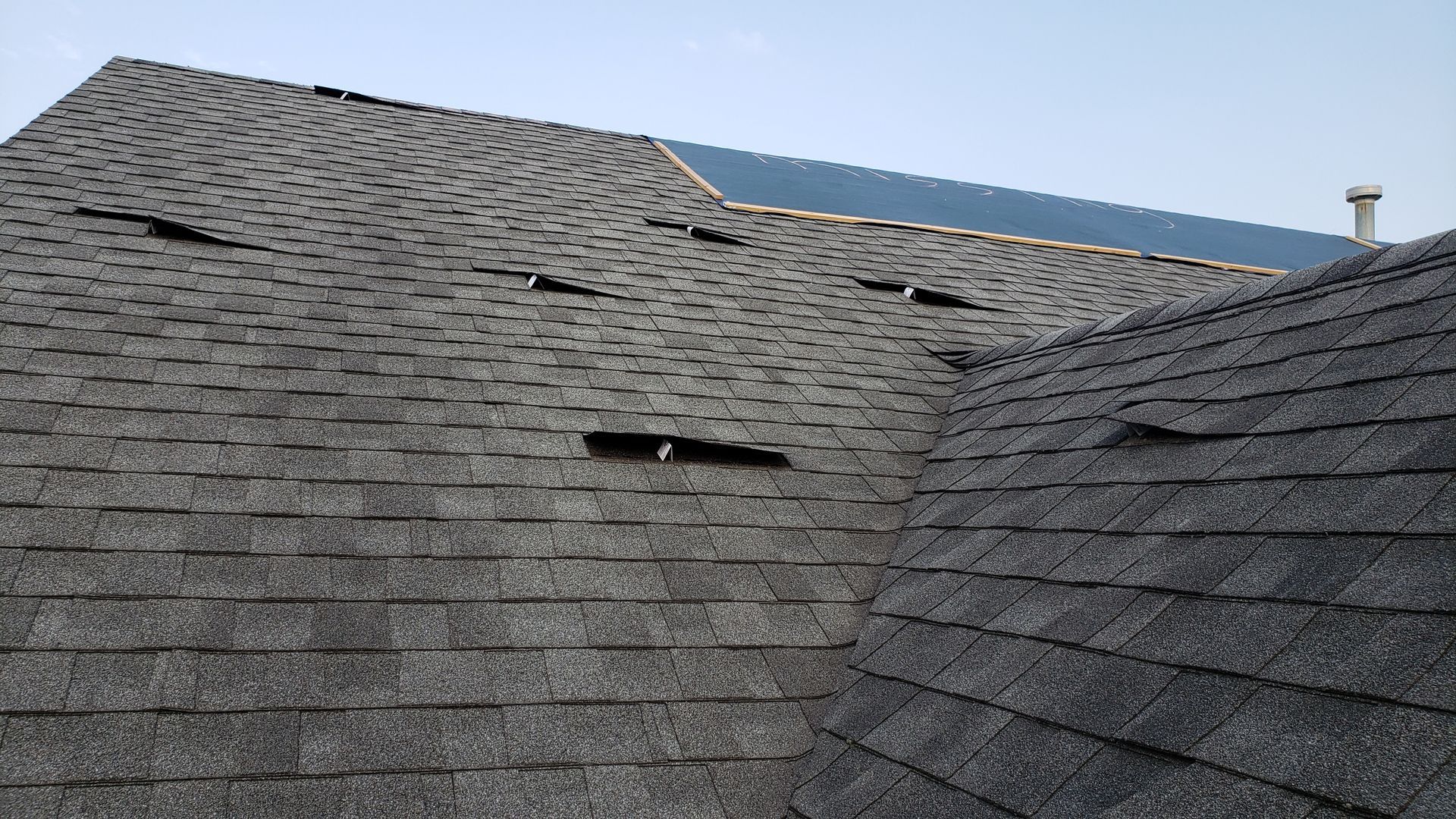 Dark gray shingled roof with two vents under a blue sky.