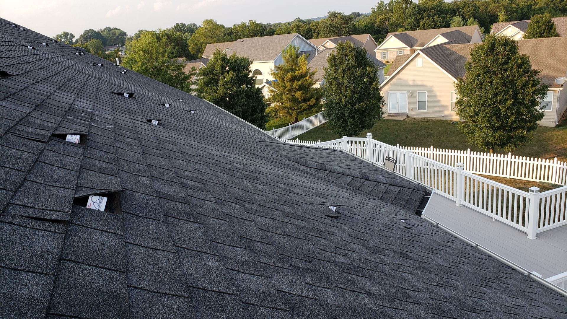 Dark gray shingled rooftop overlooking white fenced suburban houses at sunset