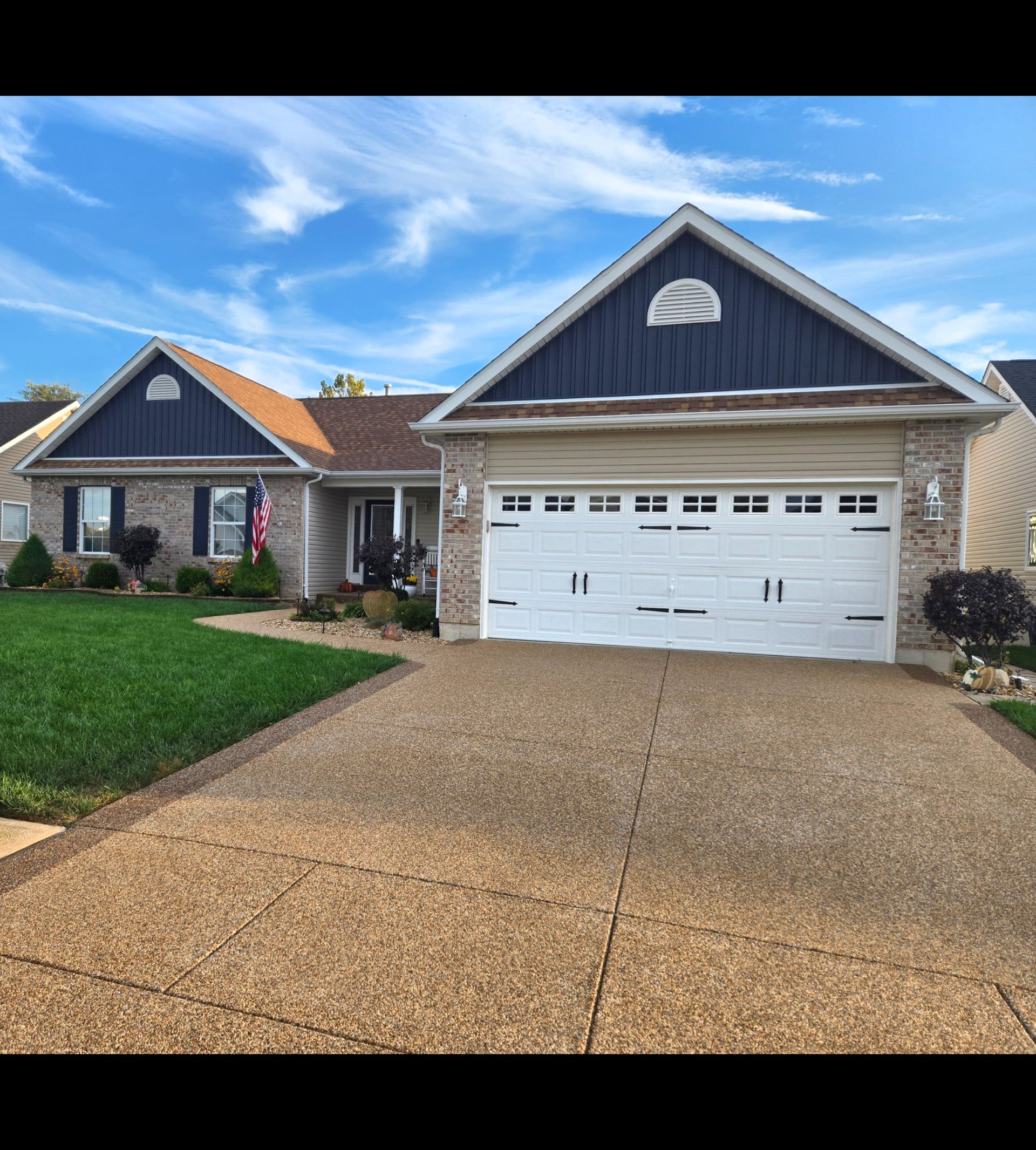A beige, single-story suburban house with blue gables, a white garage door, a concrete driveway, and a manicured lawn.