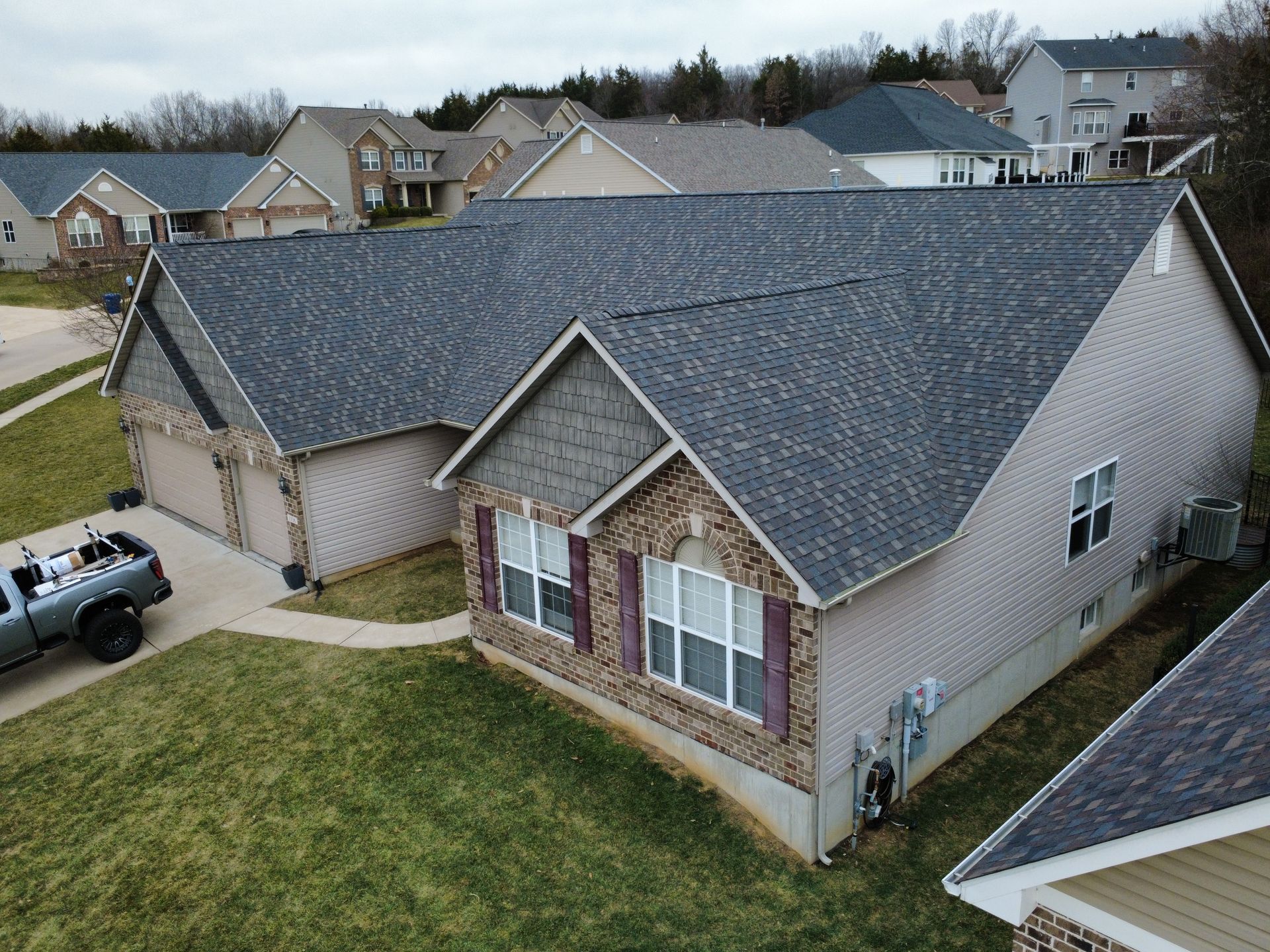 Aerial view of a suburban brick house with a gray roof and a driveway