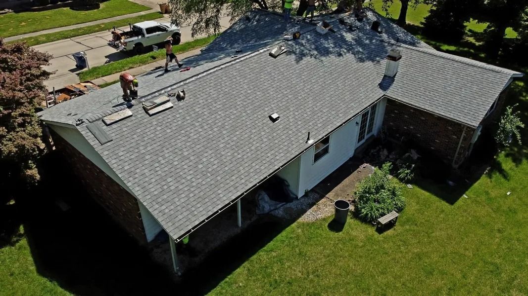 An aerial view of roofers installing gray shingles on a residential home on a sunny day.