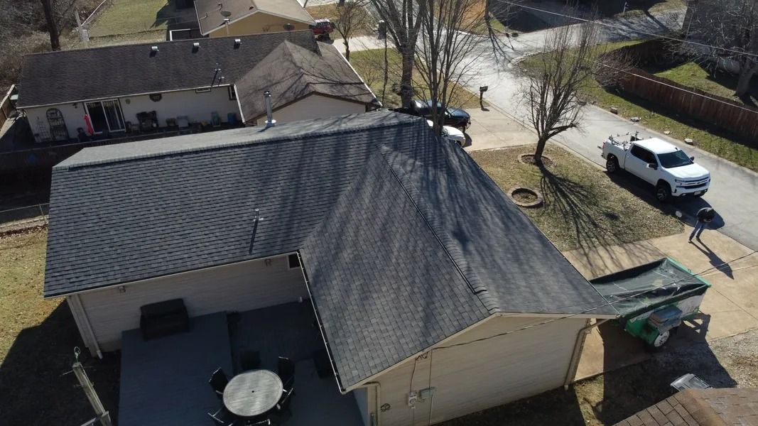 An aerial view of a tan house with a dark shingled roof, a deck with furniture, and a white truck parked in the driveway.