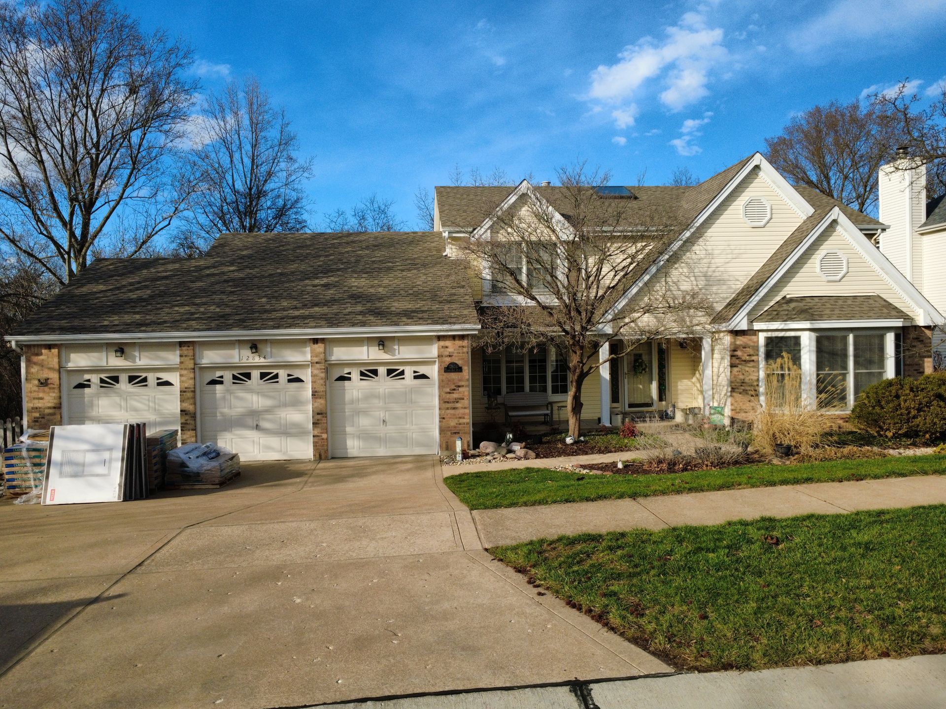 Suburban house with three-car garage, driveway, and leafless trees under a clear blue sky