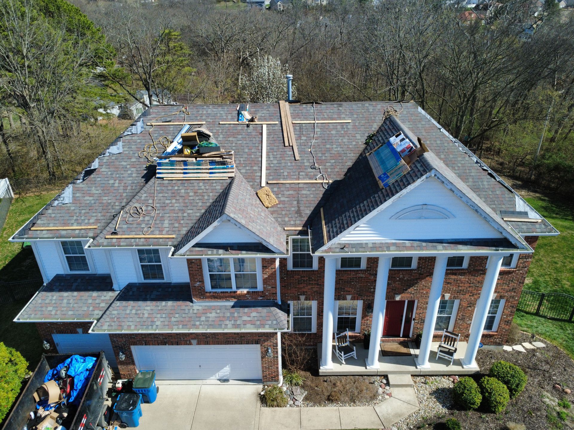 Aerial view of a brick suburban house with a gray roof, white columns, and a driveway on the left