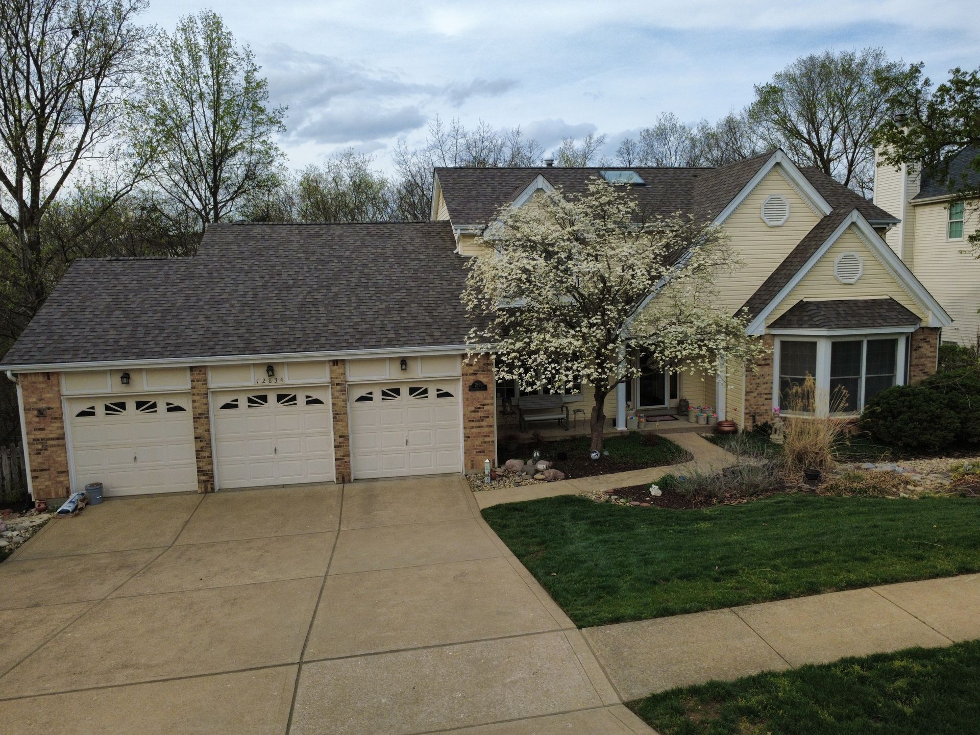 Suburban house with three-car garage, driveway, and front yard trees in spring