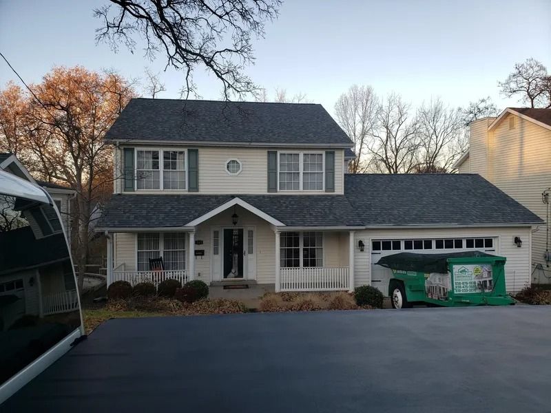 Suburban two-story house with attached garage and a green dumpster in the driveway at dusk