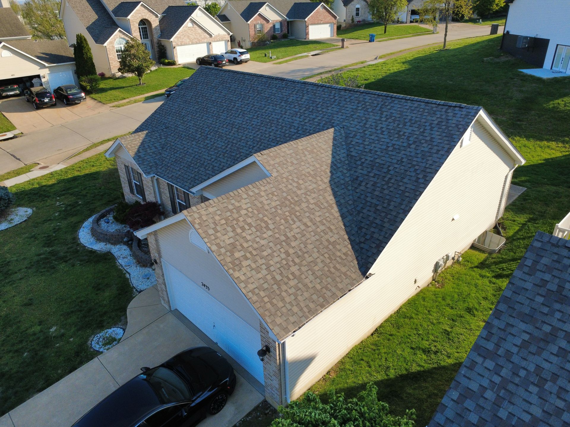 Aerial view of a suburban house with a dark roof, white siding, and a car parked in the driveway.