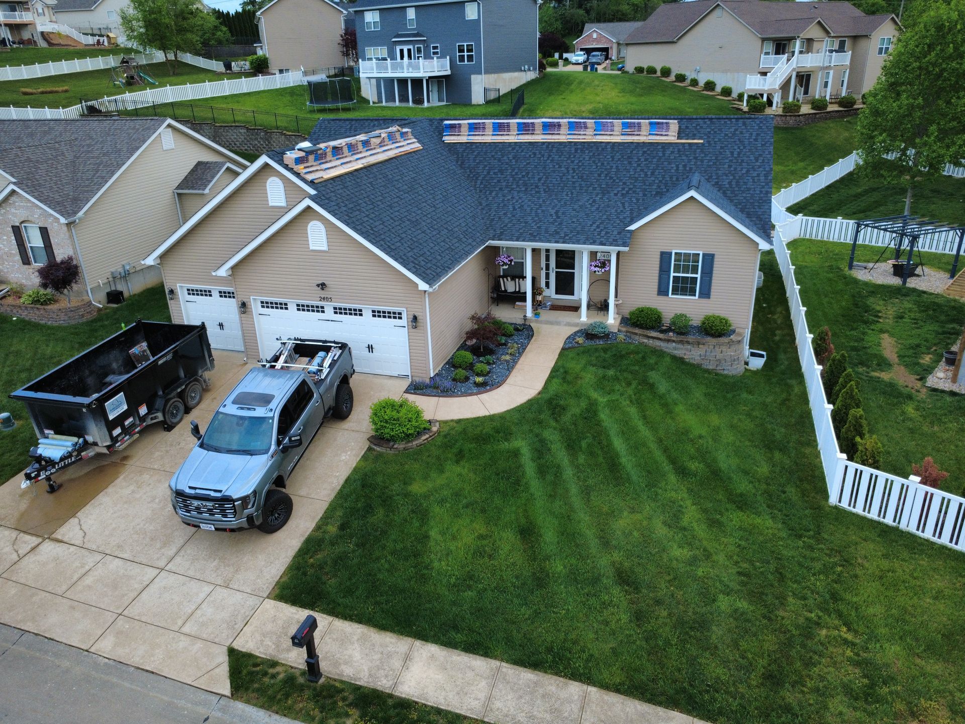 Suburban house with blue roof, driveway trucks, and a large green lawn viewed from above