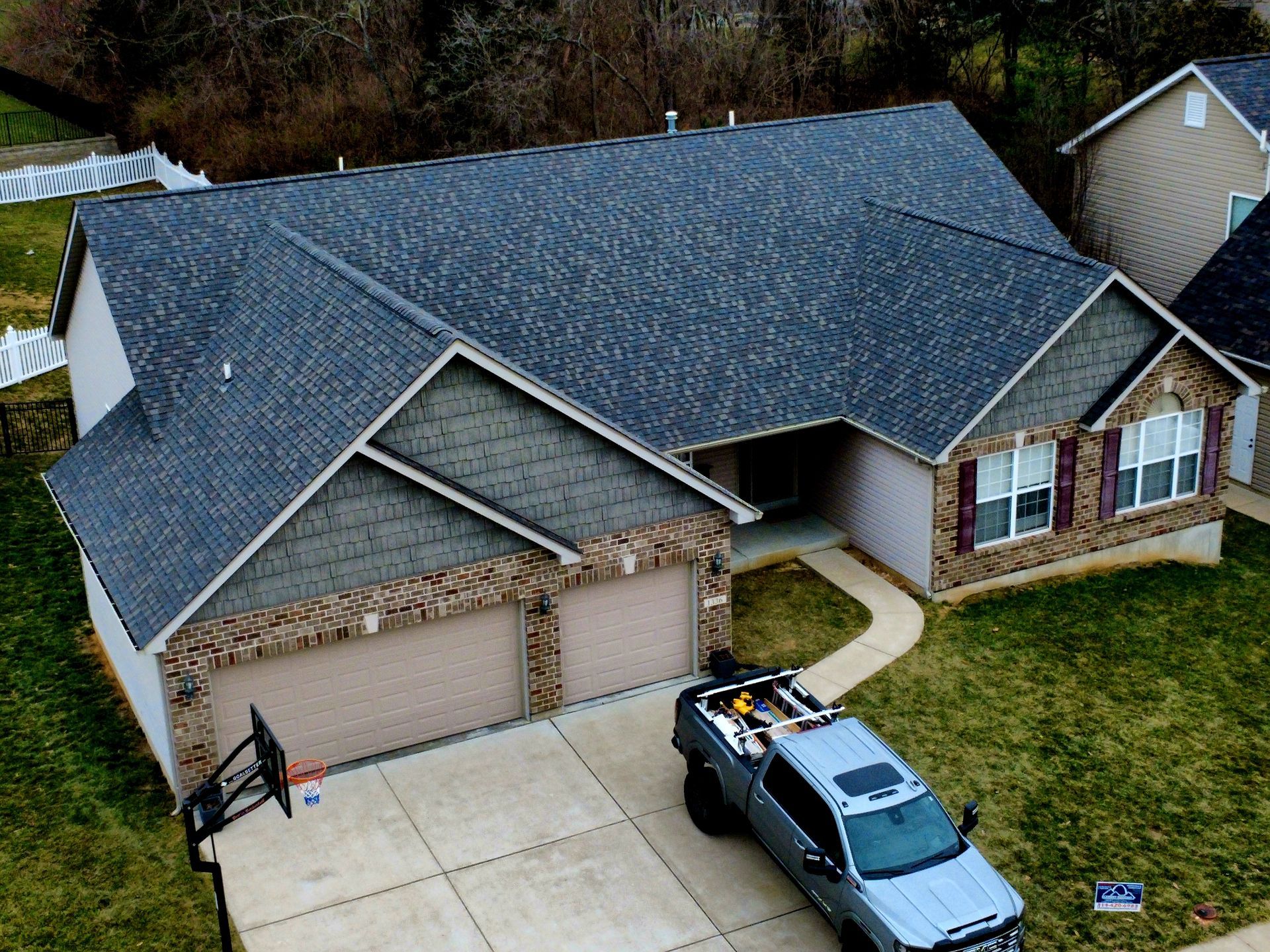Aerial view of a gray-roofed suburban house with a two-car garage and a pickup truck in the driveway.