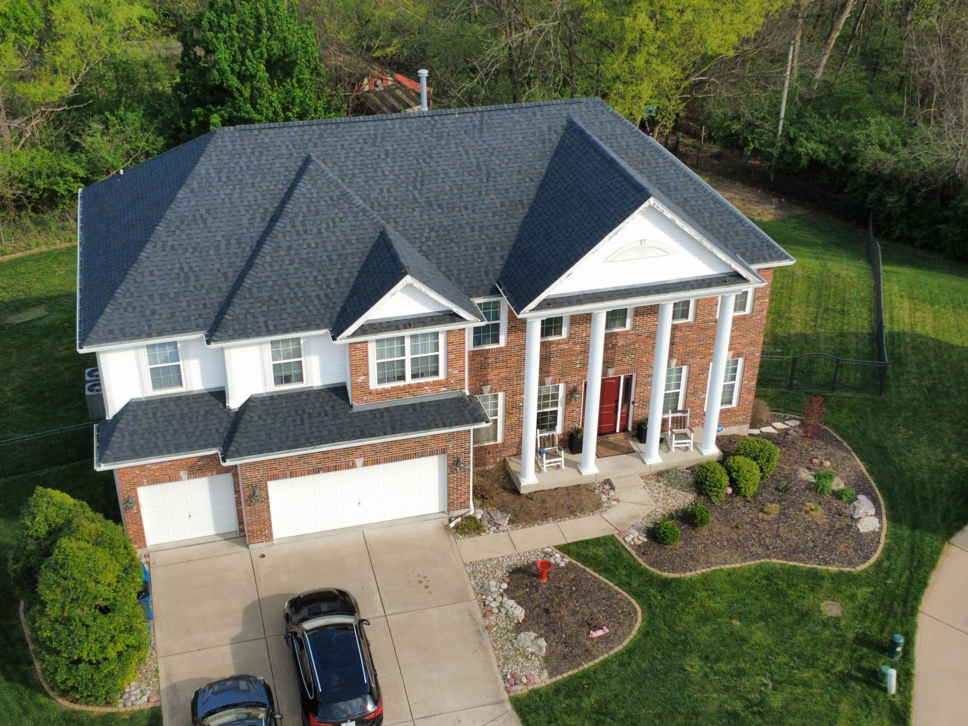 Aerial view of a two-story brick house with a dark roof, driveway, and landscaped yard