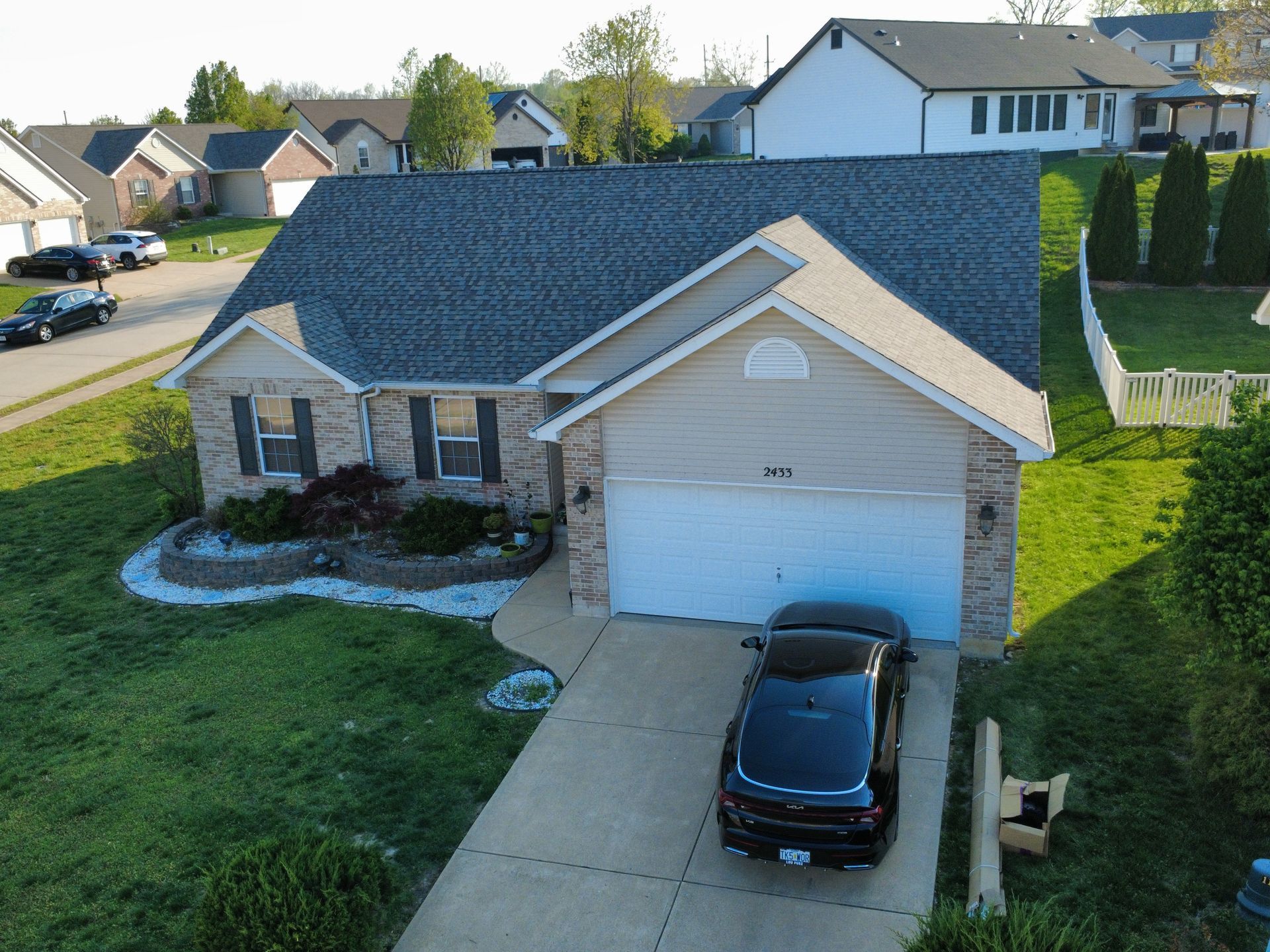Suburban house with gray roof, white garage, and black car in the driveway