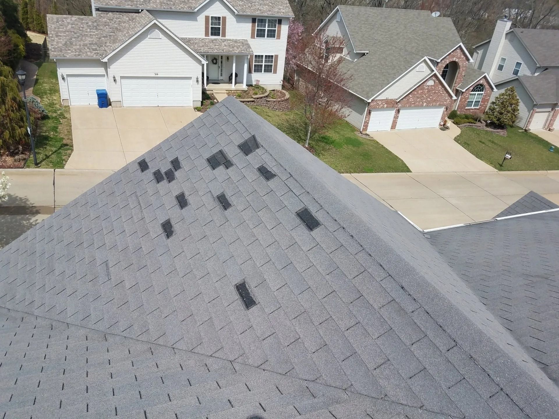 A steep residential roof with grey shingles has multiple missing shingles, exposing the dark underlayment.