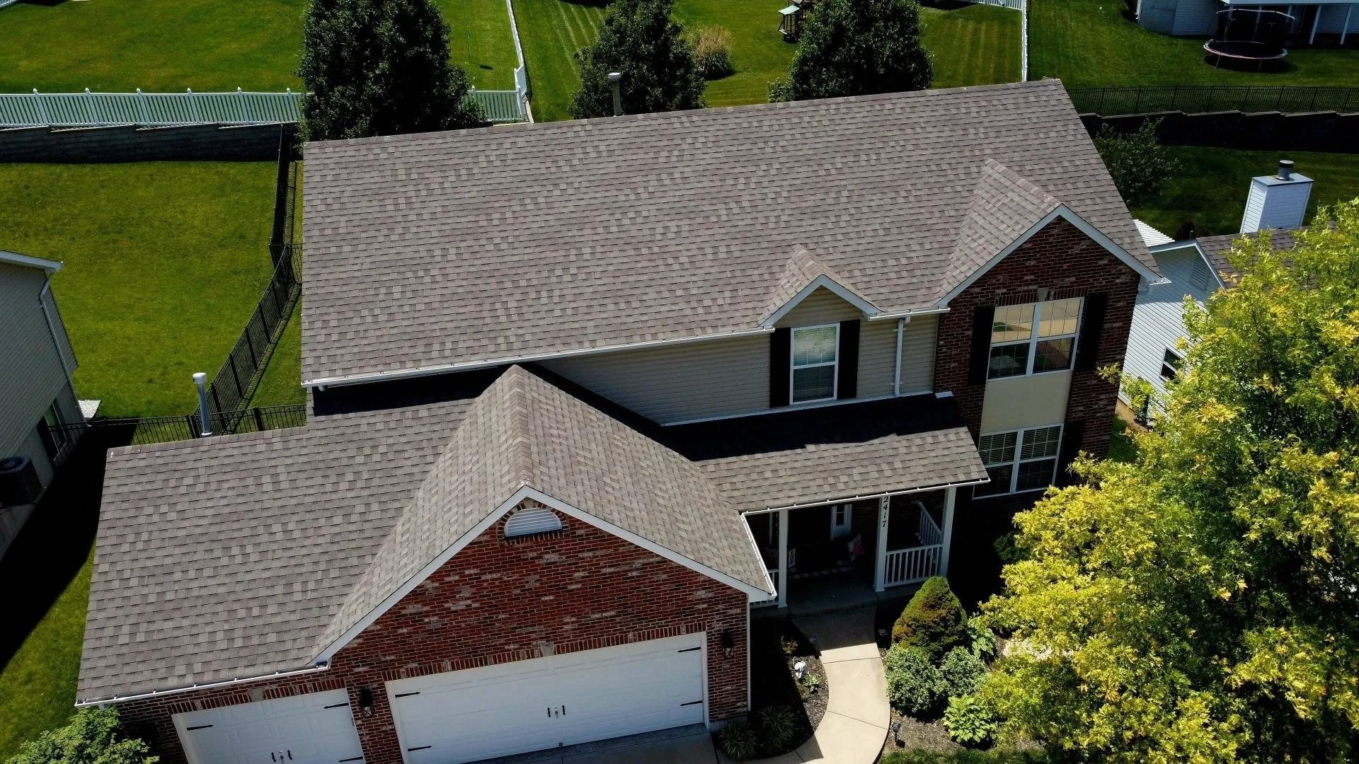Aerial view of a two-story suburban house with a gray shingled roof, red brick accents, and a front garage.