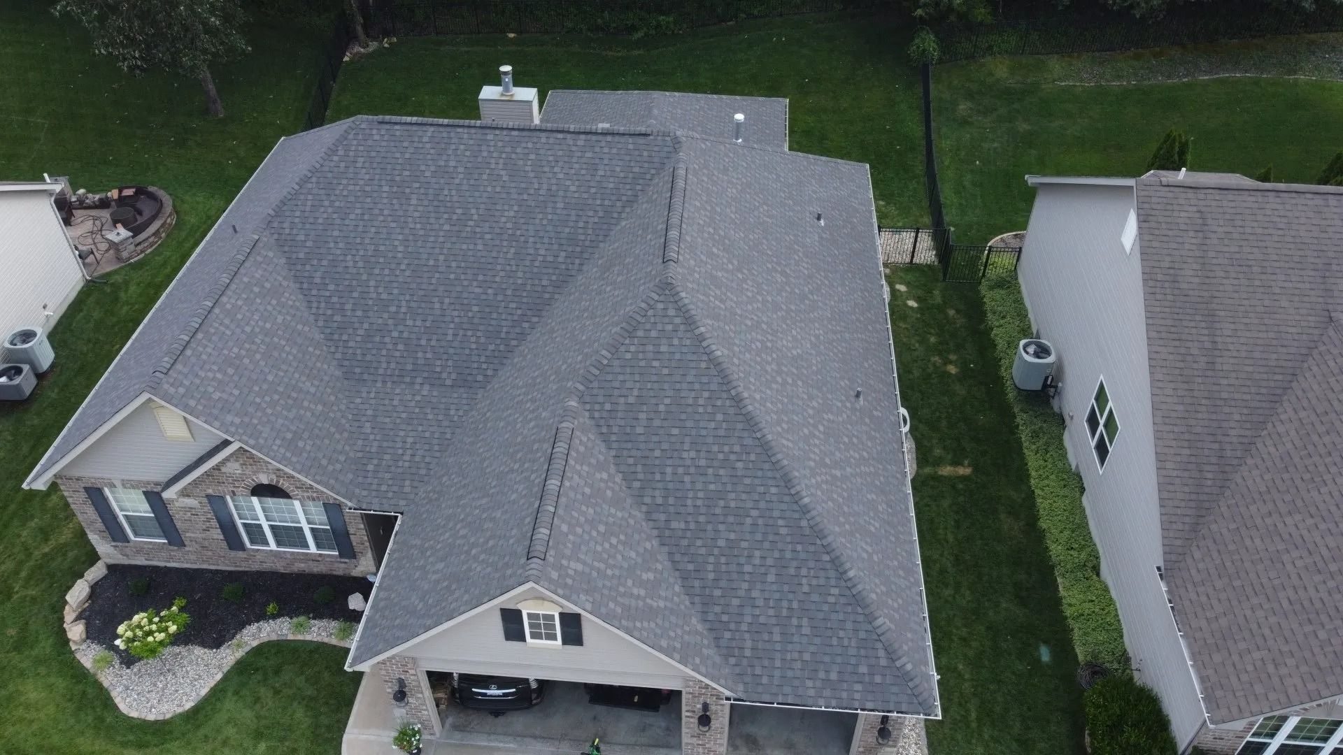An aerial view of a gray-shingled residential roof, showing the gables, a chimney, and parts of two neighboring houses.