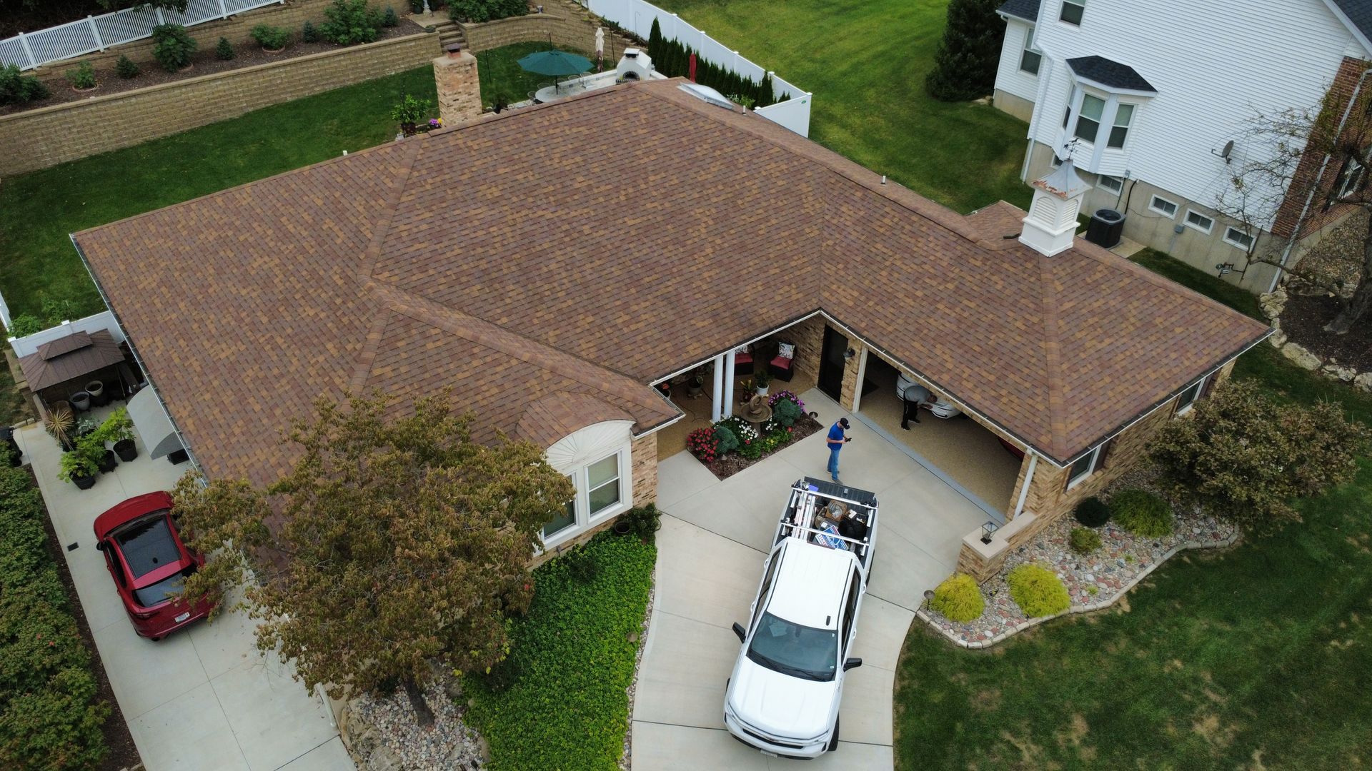 Aerial view of a residential house with a brown shingled roof, a driveway with a white truck, and a lawn.