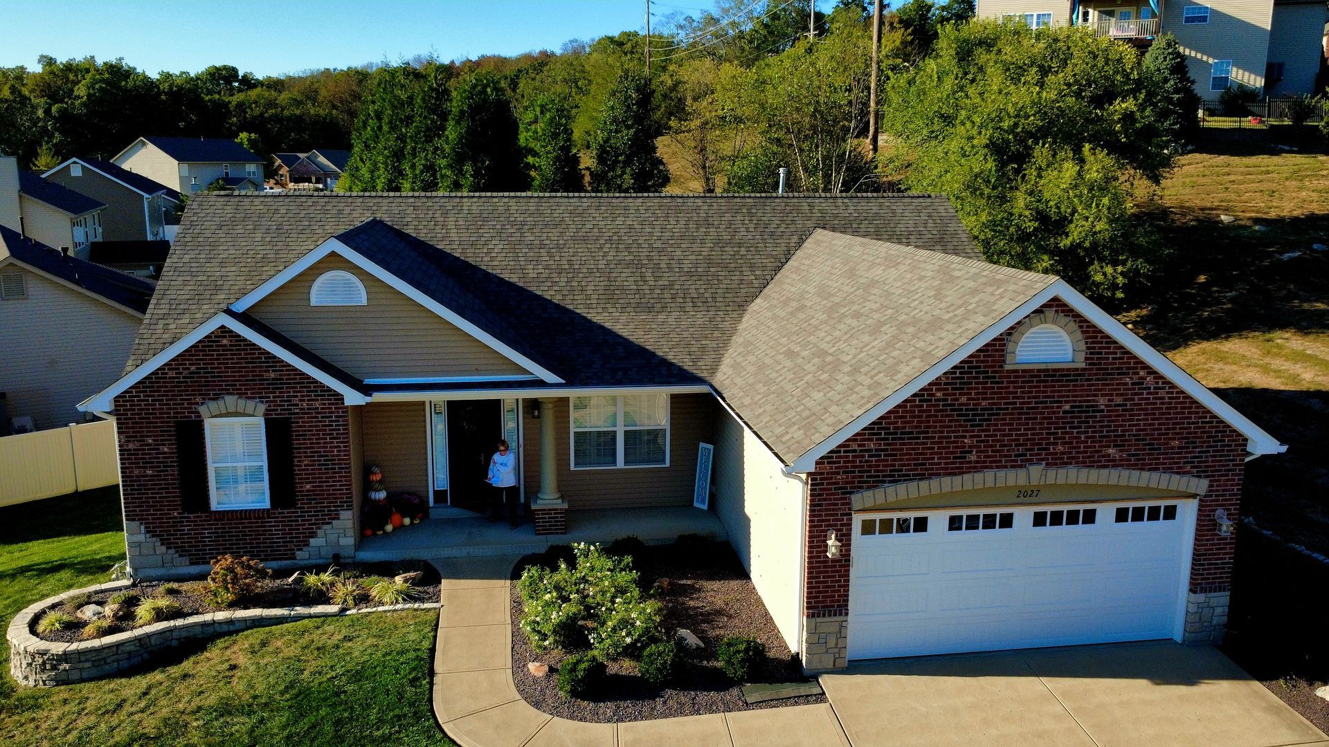 An aerial view of a single-story suburban house with a brick exterior, a garage, and a landscaped front yard.