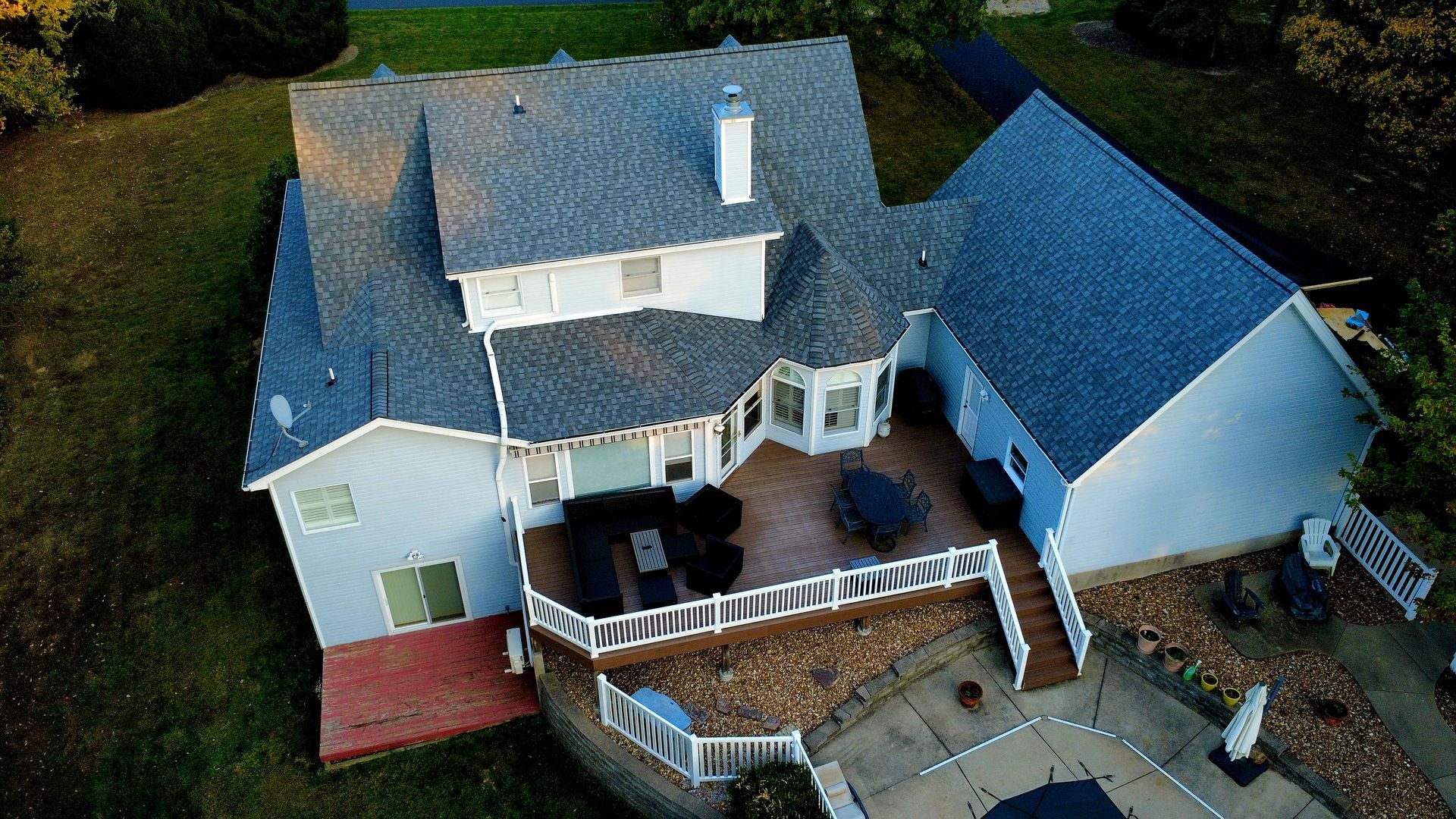 Aerial view of a two-story home with a blue roof, light siding, a spacious wooden deck, and a backyard patio.