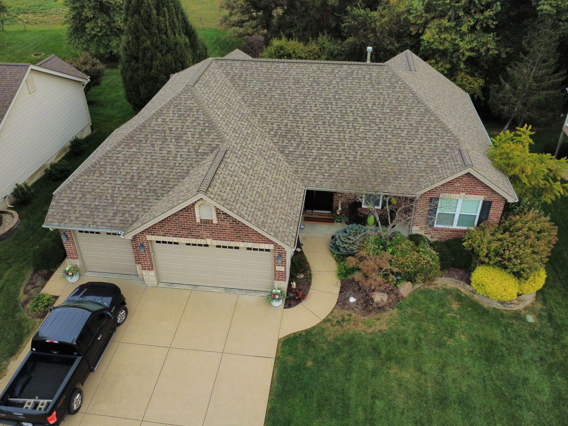 An elevated view of a single-story brick house with a tan garage and a black pickup truck parked in the driveway.