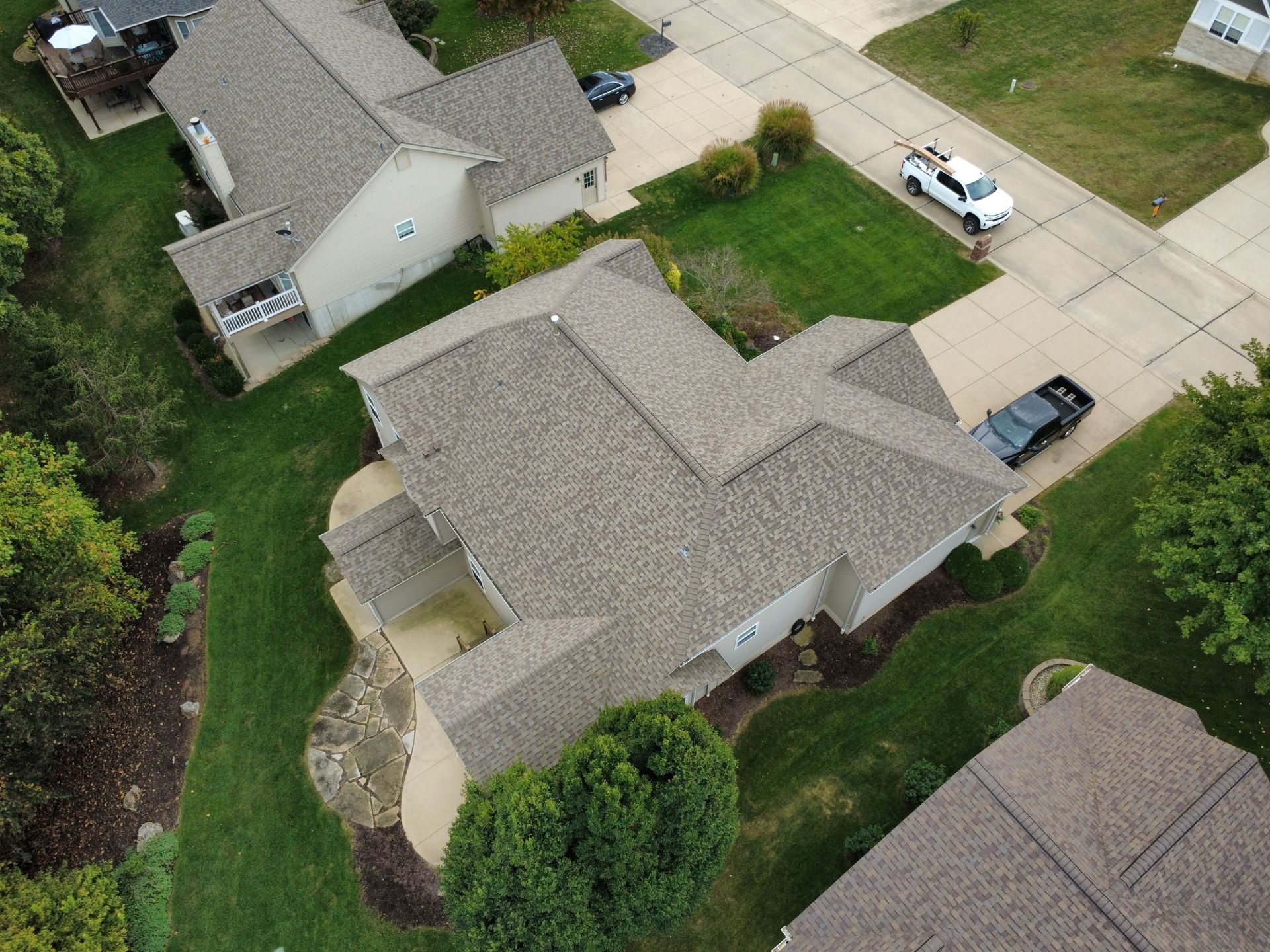 An aerial view of a suburban neighborhood showing multiple homes with shingled roofs, driveways, and green lawns.