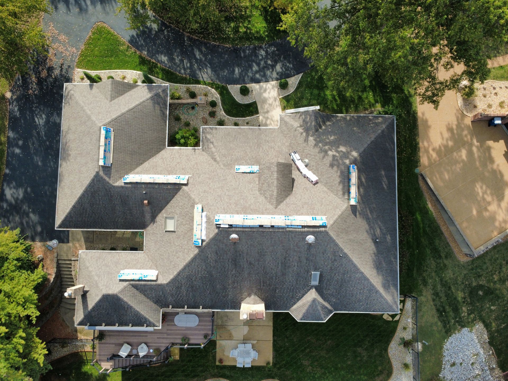 An aerial view of a shingled residential roof with several bundles of roofing materials laid out across it.