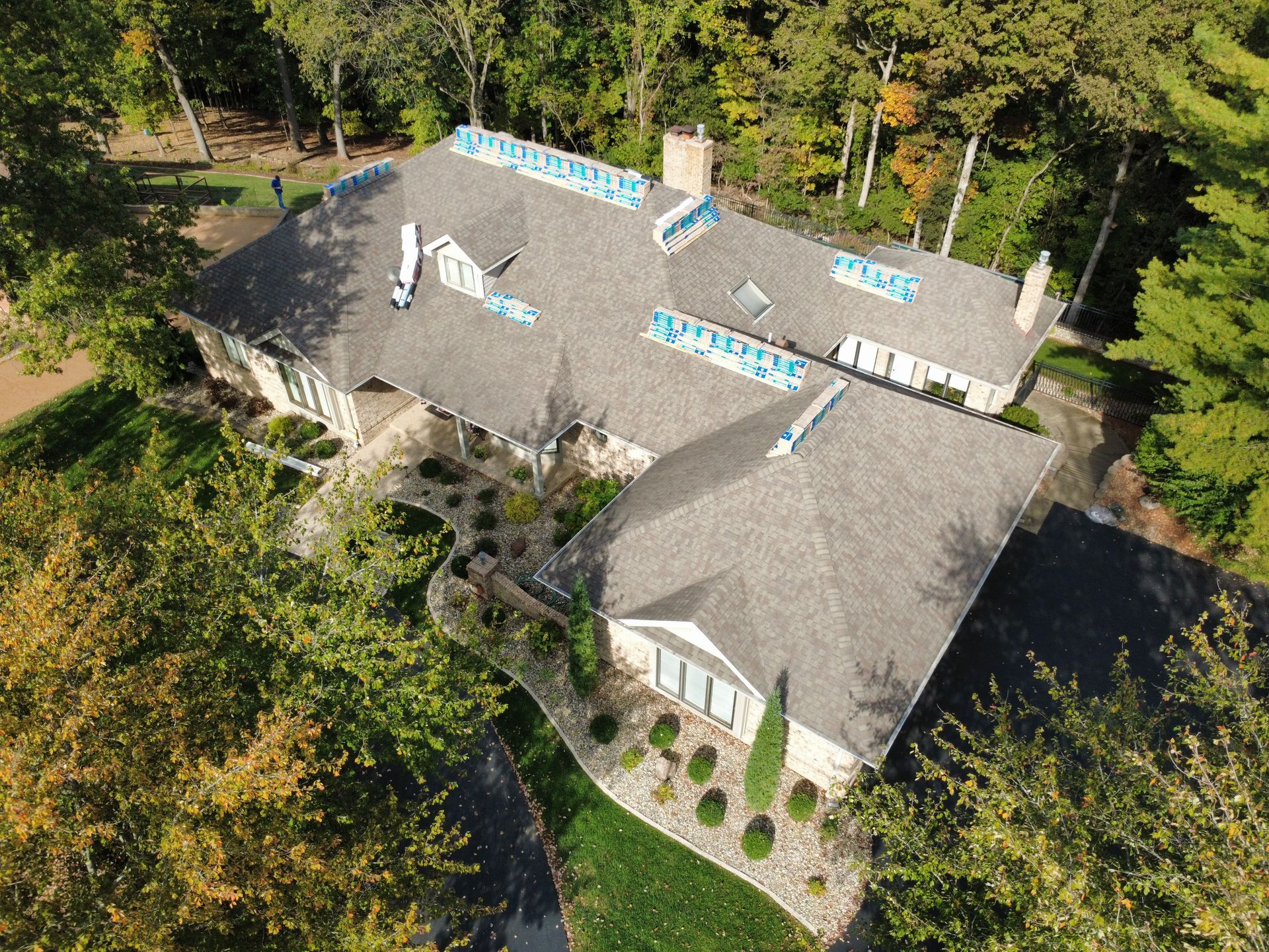 Aerial view of a house roof showing sections of blue tarps covering areas currently undergoing repair or construction.