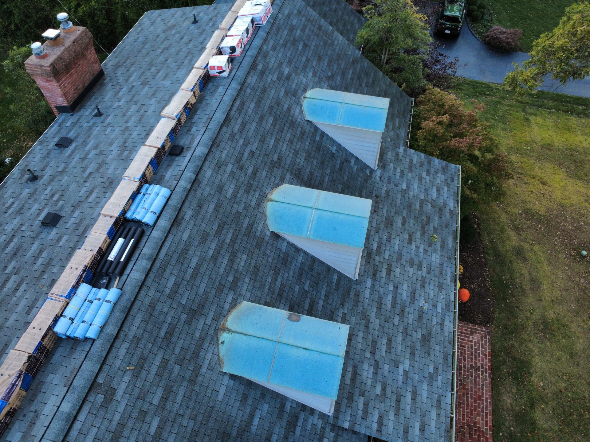 An aerial view of a residential roof undergoing repair, featuring three light blue skylights and piles of shingles.