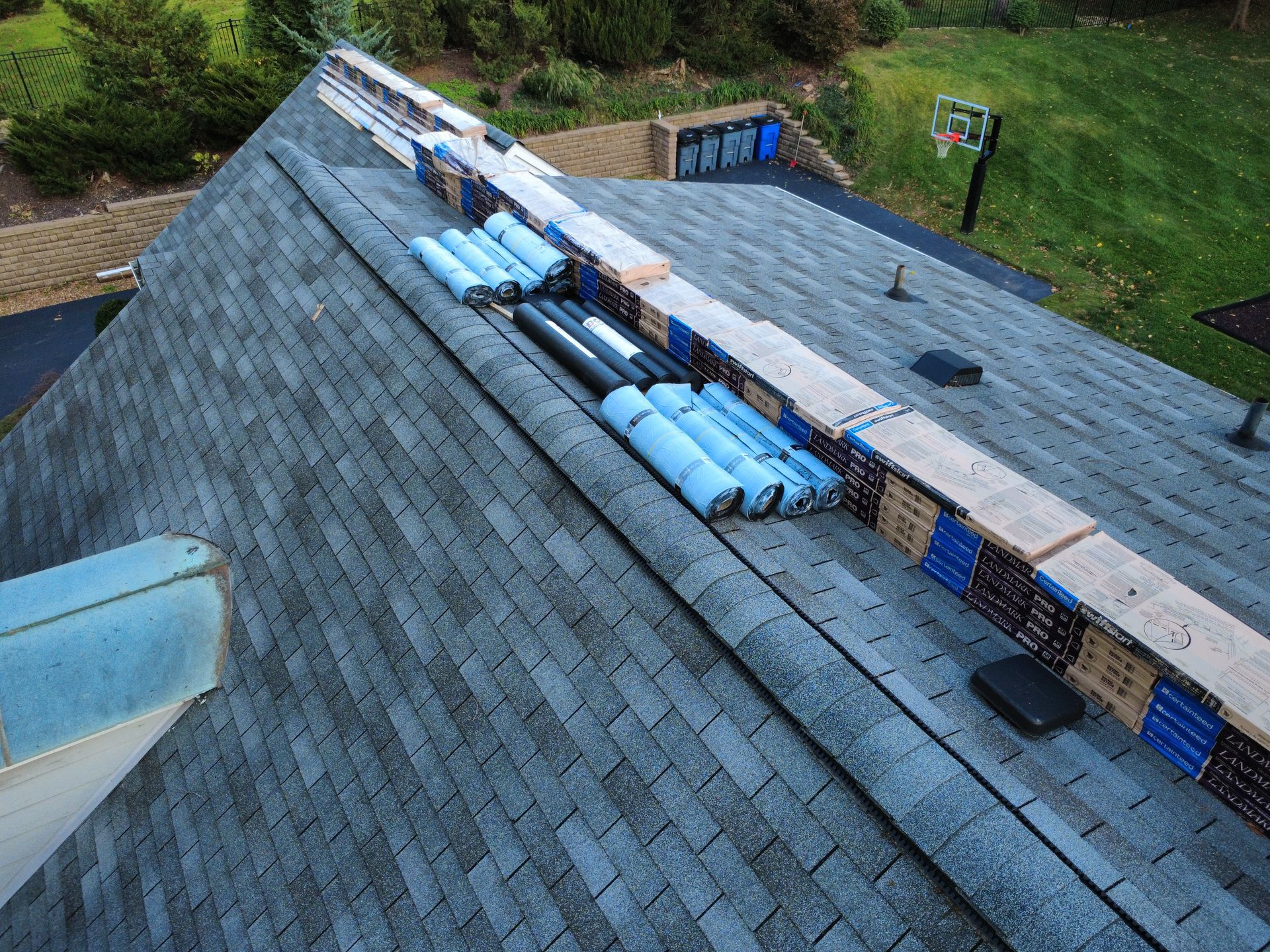Bundles of roofing shingles and felt underlayment stored along the ridge of a residential asphalt shingle roof.