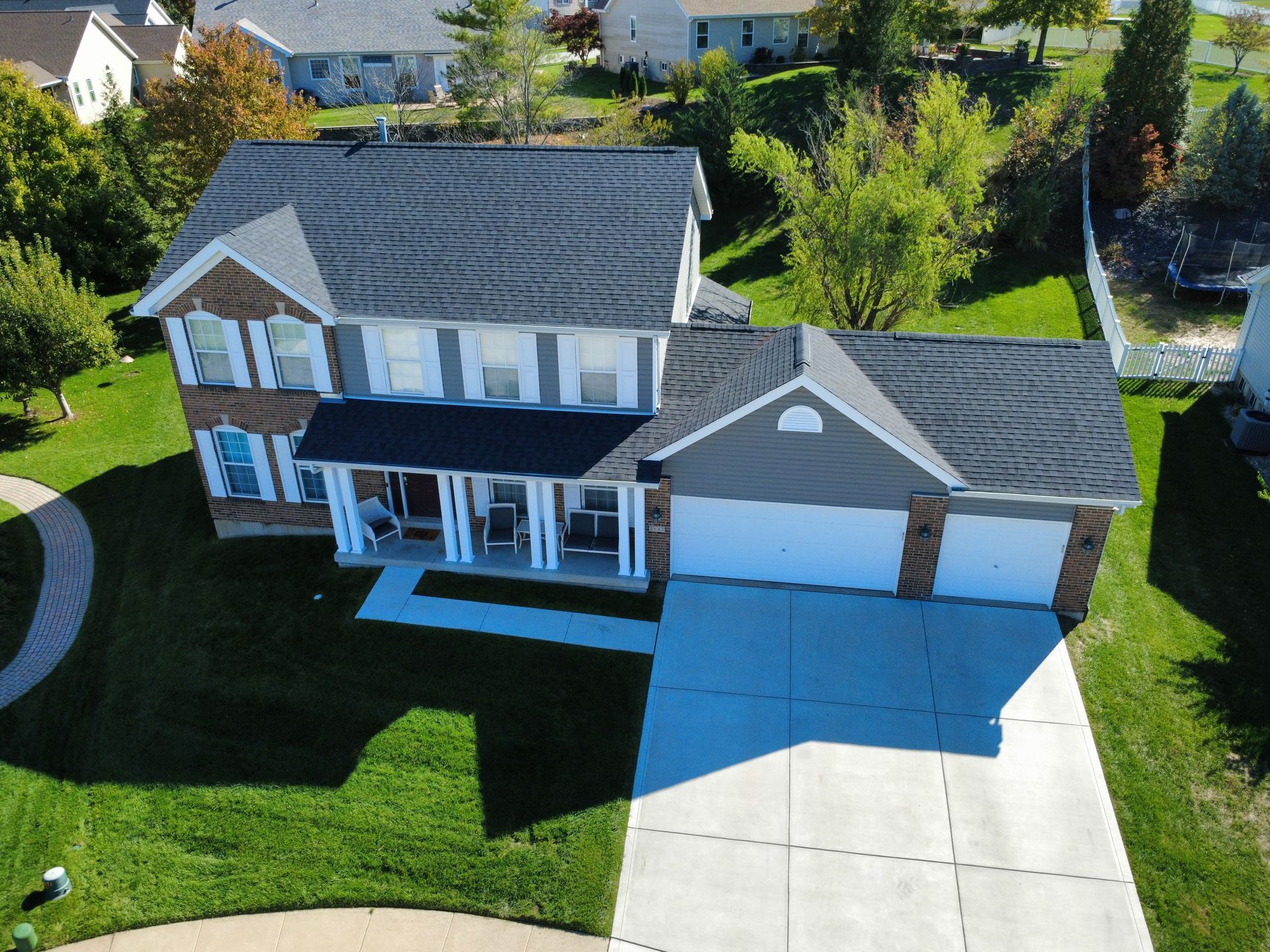 Aerial view of a two-story suburban house with a dark shingled roof, light siding, a brick facade, and a concrete driveway.