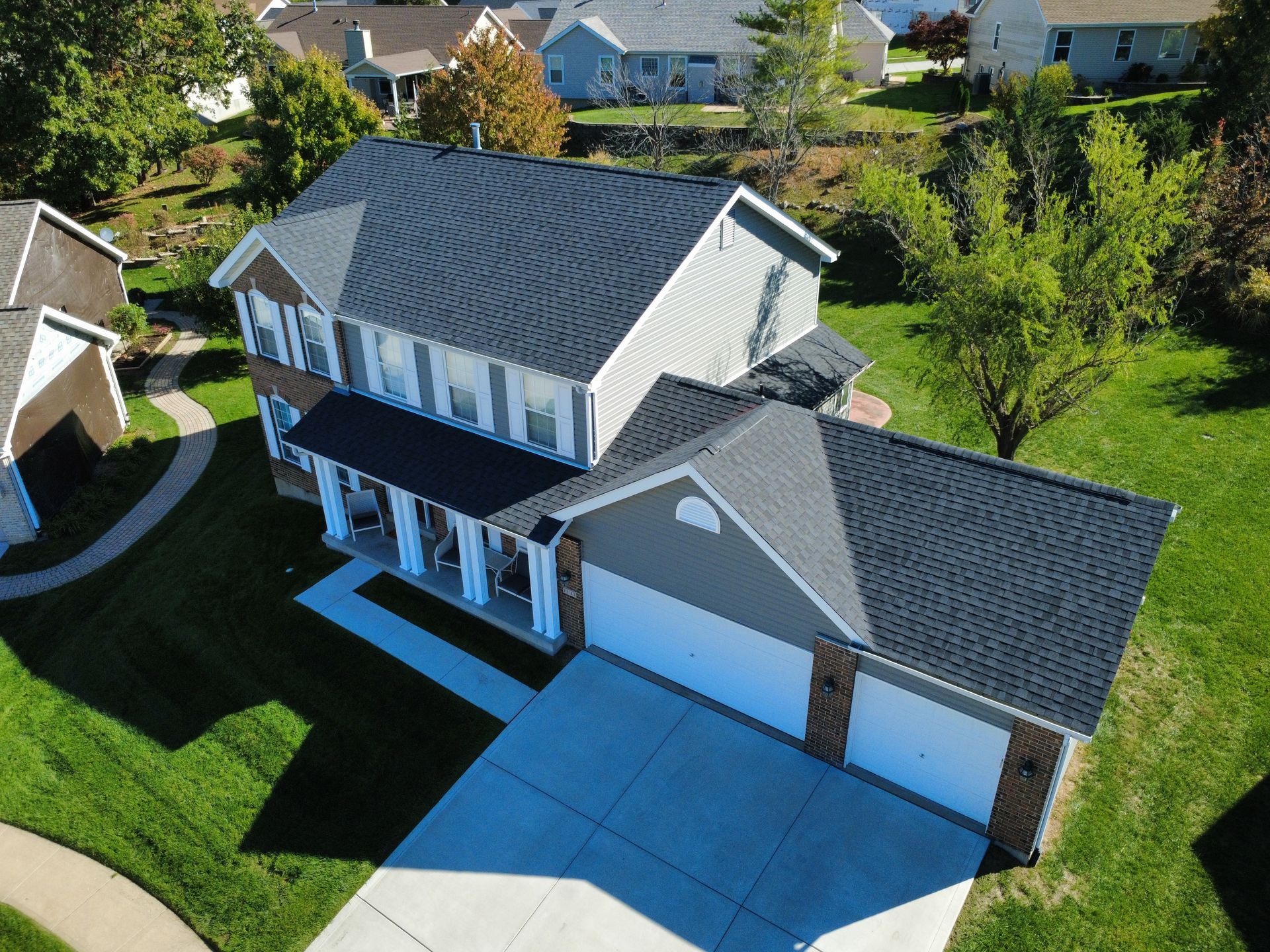 Aerial view of a two-story suburban house with a dark shingled roof, front porch, and a two-car garage.