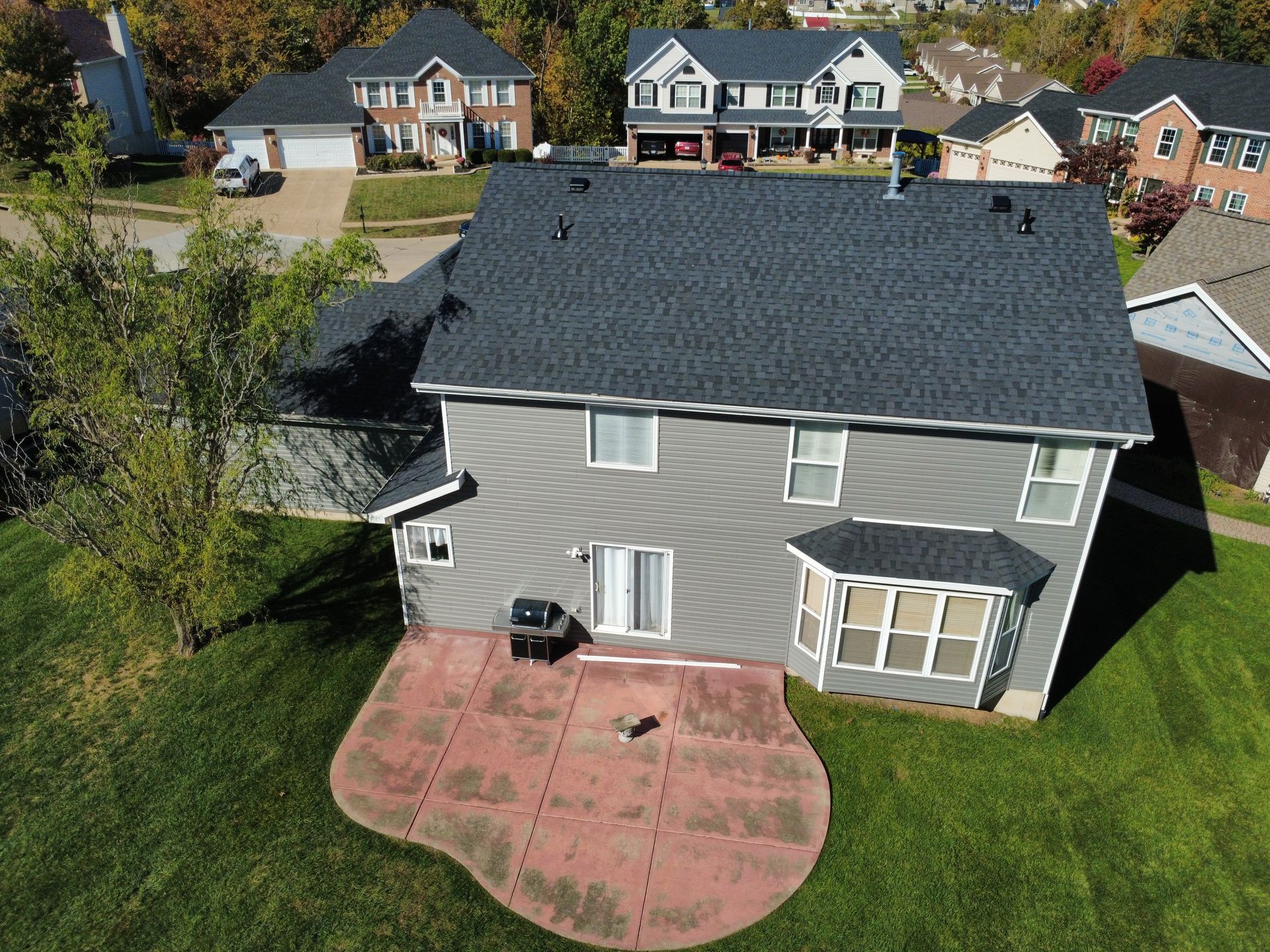 Aerial view of a gray two-story suburban house with a dark roof and a red stamped concrete patio in the backyard.